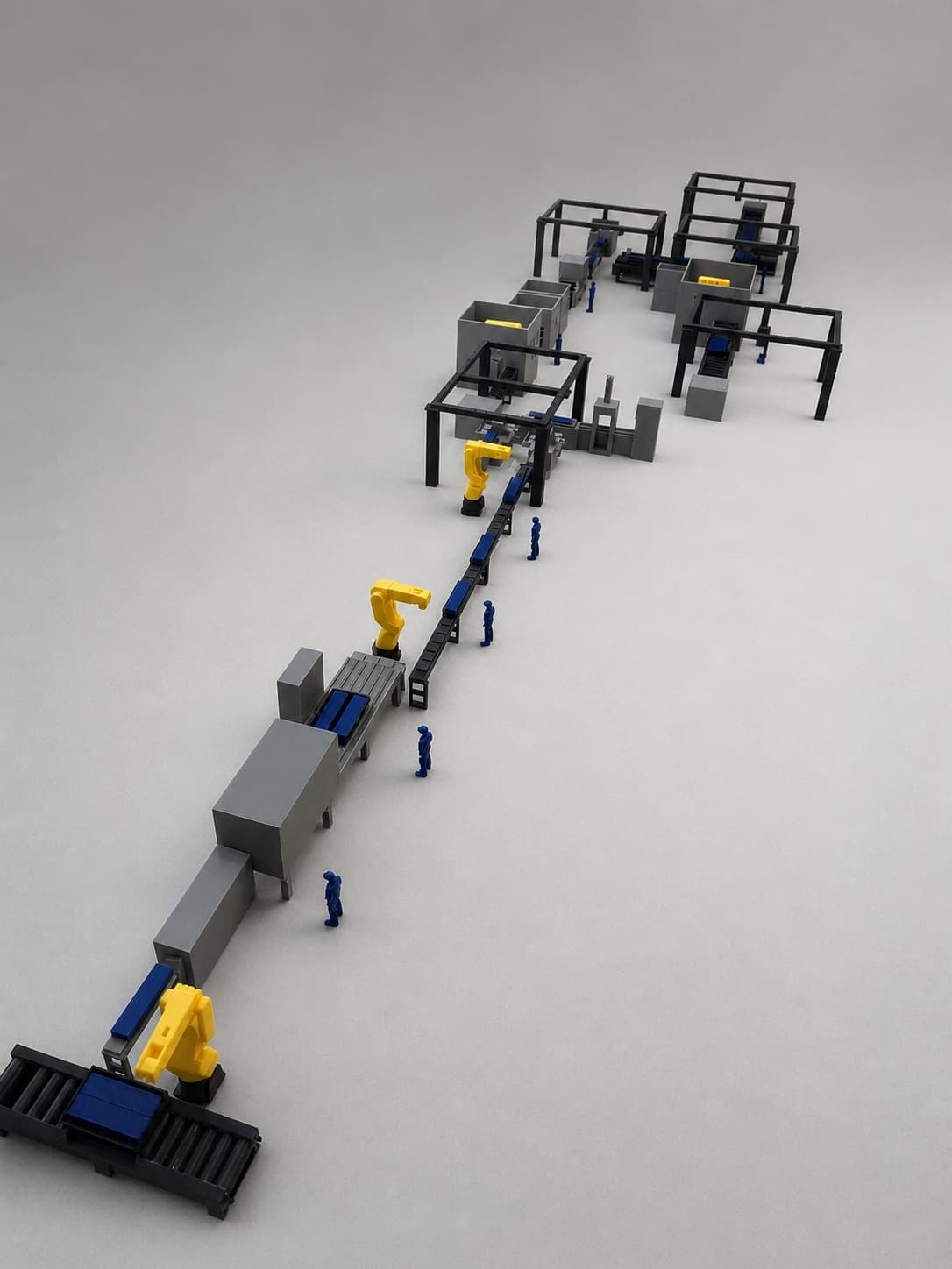 Reverse perspective of the factory scale model showing robotic arms and the production line continuing between work cells.