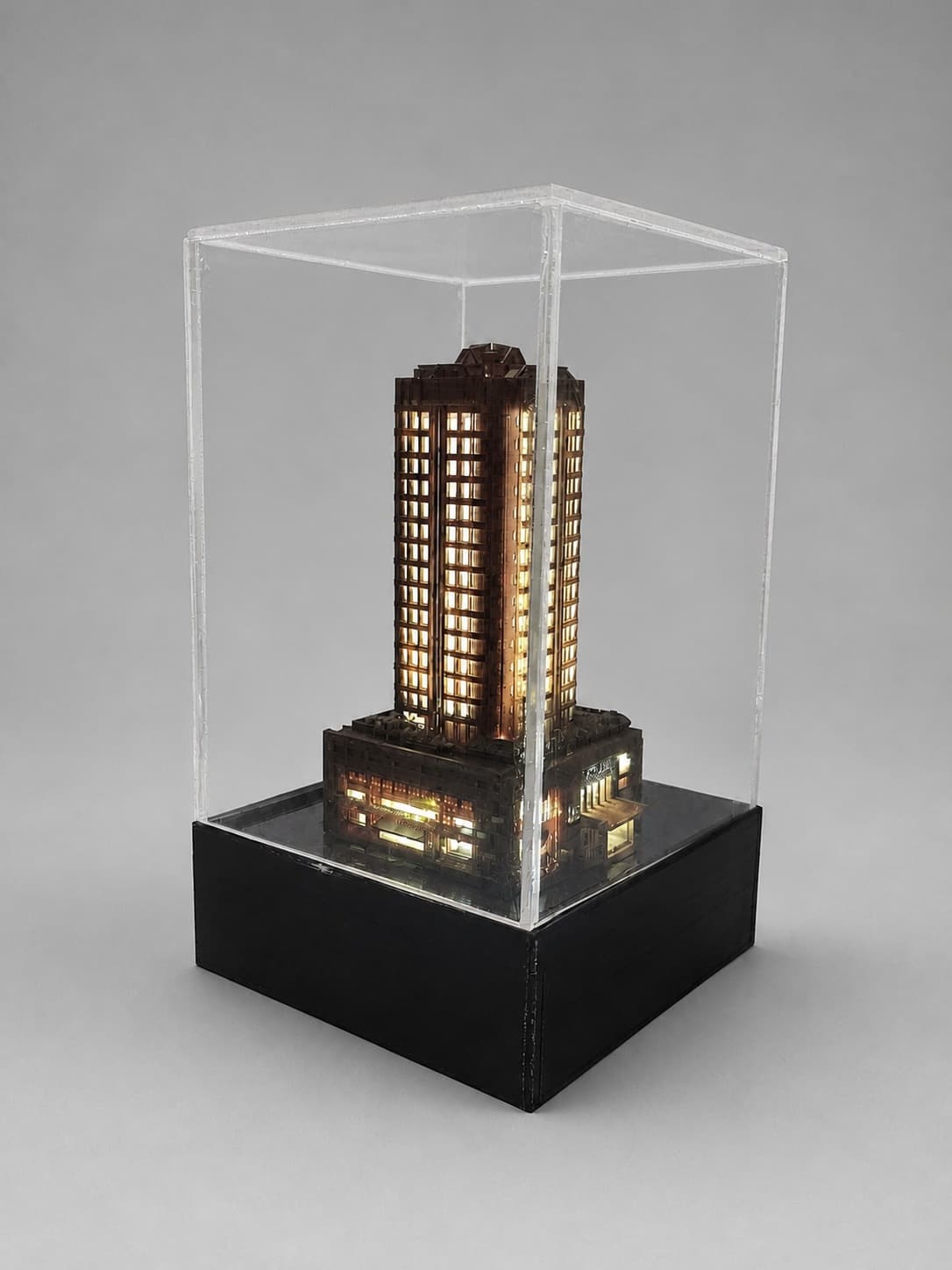 Illuminated resin apartment-building model on its black electronics base inside a clear acrylic display cover.